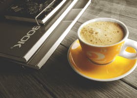 A warm cup of coffee on a yellow saucer beside a stack of books, perfect for a relaxing break.