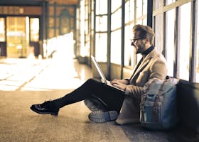 Man sitting by a window at a Budapest train station, working on his laptop with sunlight streaming through.