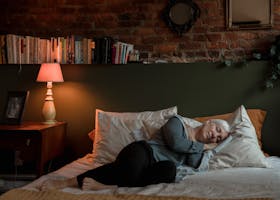 Elderly woman peacefully sleeping in a cozy bedroom with a lamp and books at night.