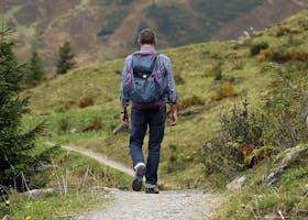 A lone hiker walks along a mountain path surrounded by lush greenery and scenic views.